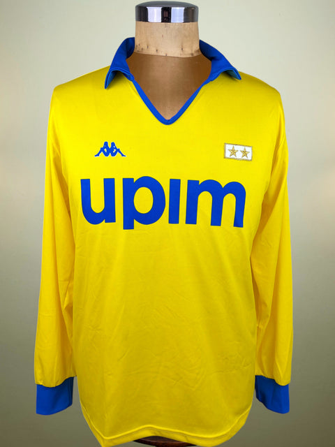 A vintage yellow long-sleeve Juventus jersey with blue collar, cuffs, and 'upim' sponsor text, displayed on a wooden mannequin torso. Features the Kappa logo on the right chest and a two-star crest on the left.