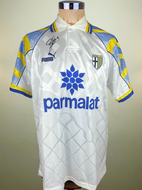 White Parma home jersey from the 1995-96 season with blue and yellow accents on a mannequin against a plain background, and the signature of Enrico Chiesa in felt-top pen above the Puma logo.