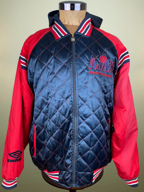 A vintage-style quilted jacket displayed on a mannequin torso. The jacket features a navy blue diamond-quilted body with red and white striped ribbed collar, cuffs, and hem, paired with bright red sleeves.