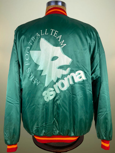 Green satin bomber jacket shown from the back on a mannequin, featuring a large white wolf logo and the text 'ASICS FOOTBALL TEAM' and 'asics' printed across the back, with red and yellow striped ribbed collar, cuffs, and hem.