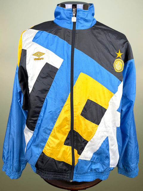 A vintage Inter Milan windbreaker jacket by Umbro, featuring a bold geometric pattern of blue, black, yellow, and white. The jacket is displayed on a mannequin torso against a neutral beige background.