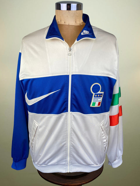 A vintage Nike track jacket displayed on a mannequin torso. The jacket is white with royal blue panels on the chest and sleeves, featuring a white Nike swoosh on the right chest, an Italian Football Association crest on the left chest, and a green, white, and red Italian flag patch on the left sleeve.