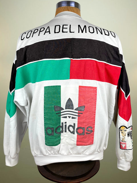 White Adidas windbreaker jacket with black, green, and red color-blocked stripes and a large Adidas trefoil logo with 'Coppa del Mondo' text on the back, displayed on a mannequin.
