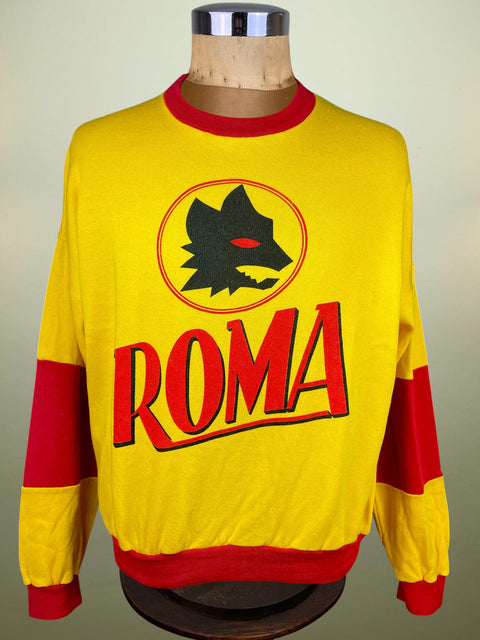 A yellow and red long-sleeve soccer sweatshirt with 'ROMA' and a wolf logo, displayed on a mannequin torso.