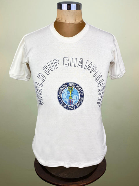 A white short-sleeve t-shirt displayed on a mannequin torso, featuring a blue and gray graphic that reads 'WORLD CUP CHAMPIONSHIP' with a central FIFA crest.
