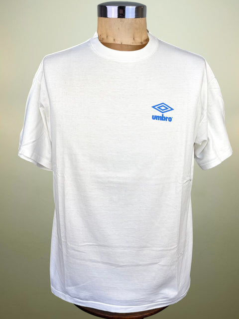 A white short-sleeve crewneck t-shirt with a blue embroidered Umbro logo on the left chest, displayed on a wooden dress form mannequin against a neutral beige background.