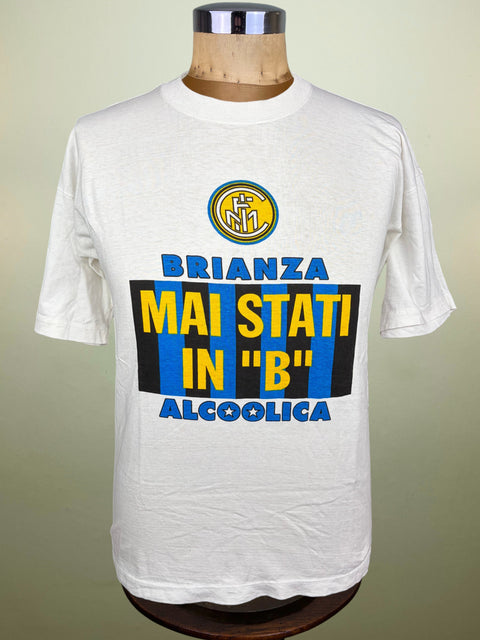 A white short-sleeve graphic T-shirt displayed on a wooden dress form mannequin. The shirt features a yellow and blue Inter Milan crest at the chest, and a large graphic in the center with the Italian phrase 'BRIANZA ALCOOLICA - MAI STATI IN B" in yellow and blue text over a black and blue striped background.
