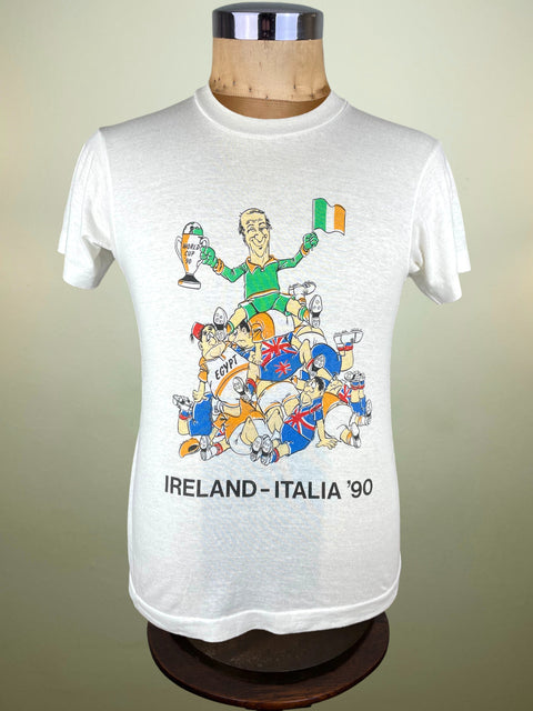 White Ireland Italia 90 T-Shirt with a colorful graphic of Jack Charlton standing on top of the England fans on a mannequin against a beige background