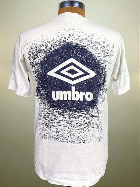 White Umbro short-sleeve t-shirt shown from the back on a mannequin, featuring a large navy blue distressed circle graphic with the white Umbro diamond logo and 'umbro' text.