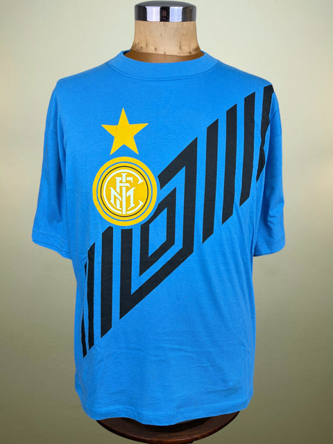 A bright blue Inter Milan soccer t-shirt displayed on a wooden dress form mannequin. The shirt features the club's yellow and white circular crest with a yellow star on the chest, and a large black geometric graphic pattern running diagonally across the front.