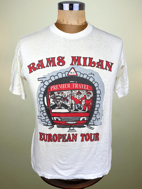 A vintage white graphic t-shirt displayed on a wooden dress form mannequin. The shirt features a large red and gray graphic print of a train and the text 'RAMS MILAN EUROPEAN TOUR'.