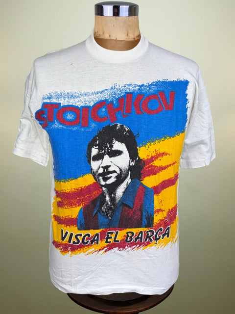 A vintage white graphic t-shirt displayed on a wooden dress form mannequin. The shirt features a colorful print with the text 'STOICHKOV' in red above a portrait of a man and a blue, yellow, and red striped background, with 'VISCA EL BARCA' written at the bottom.