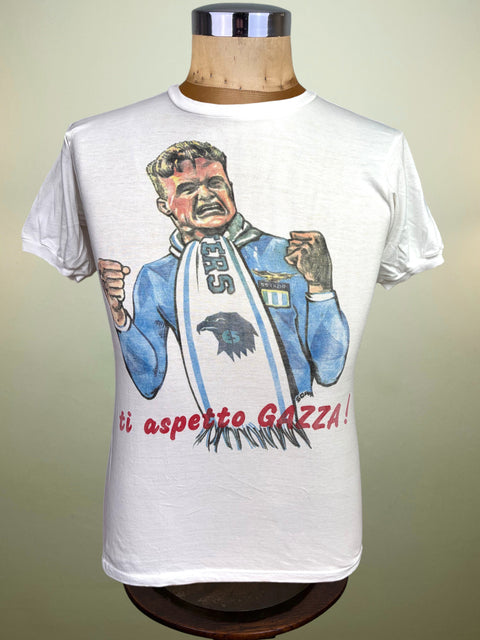 A vintage white graphic t-shirt displayed on a wooden dress form mannequin. The shirt features a colorful illustration of a football player wearing a blue jersey and a white scarf with 'Gazza' written in red text below.