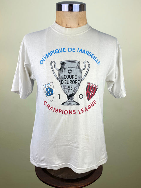 White t-shirt with Olympique de Marseille Champions League design on a mannequin against a beige background