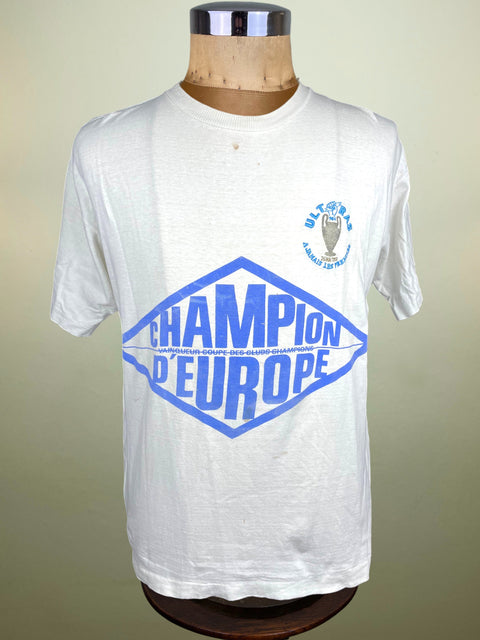 White t-shirt with blue text and logo on a mannequin against a beige background