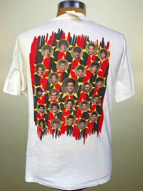 A vintage white short-sleeve t-shirt displayed on a mannequin, showing the back side with a large graphic print of the AC Milan football team in red, black, and yellow with circular player portraits.
