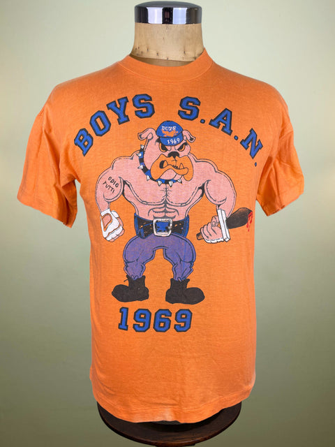 Orange Inter Milan Boys Ultras Group t-shirt with graphic design of a muscular cartoon character and text saying BOYS S.A.N. 1969 on a mannequin against a beige background.