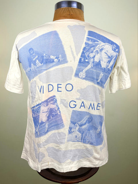 A vintage off-white graphic t-shirt displayed on a wooden mannequin torso, showing the back of the shirt with blue video game-themed collage graphics of Faustino Asprilla and the text 'VIDEO GAME'.