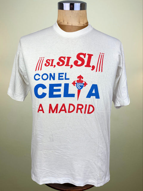 A white short-sleeve graphic T-shirt displayed on a wooden dress form mannequin against a light beige background. The shirt features a bold red and blue graphic with the Spanish text 'SI, SI, SI, CON EL CELTA A MADRID' and a central Celtic cross and bird emblem.