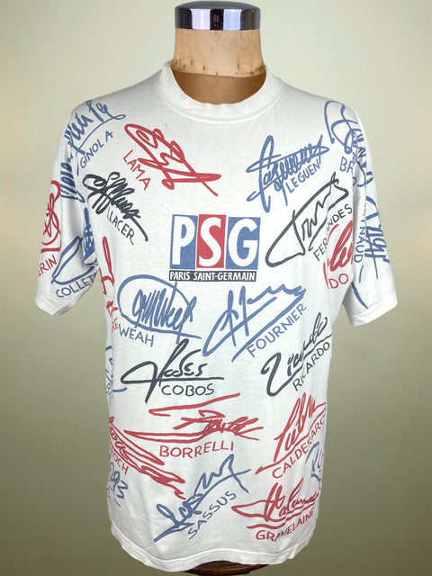 White t-shirt with various signatures and a PSG logo on a mannequin against a beige background