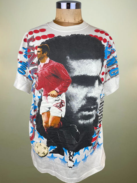 T-shirt with a graphic design of a soccer player and a face, on a mannequin against a beige background.