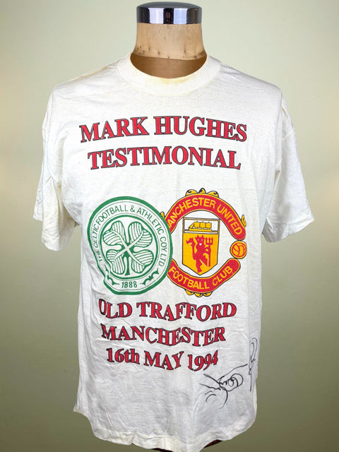 A white short-sleeve graphic T-shirt displayed on a wooden dress form. The shirt features red text reading 'MARK HUGHES TESTIMONIAL' and 'OLD TRAFFORD MANCHESTER 16TH MAY 1994', along with green and red Manchester United and West Ham crest graphics.