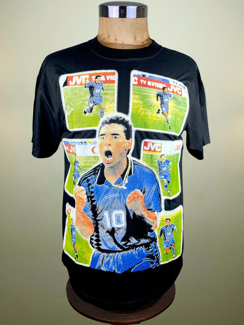 Black t-shirt with a graphic design of a Diego Maradona scoring for Argentina in World Cup 1994 and JVC branding on a mannequin against a beige background.