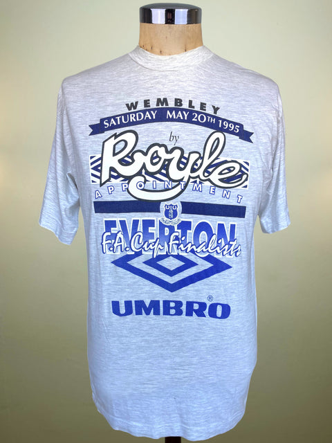 A light gray heather crewneck t-shirt displayed on a wooden dress form mannequin. The shirt features a large blue and white graphic print celebrating the 1995 FA Cup Final at Wembley, featuring the Umbro brand logo.