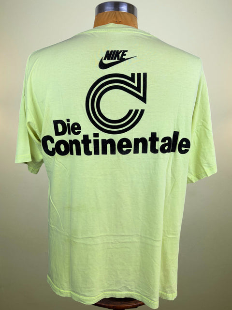 A light neon yellow-green Nike t-shirt displayed on a wooden mannequin torso, showing the back with a large black graphic of the Continental 'C' logo and the Nike swoosh.