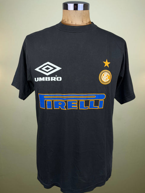 A black Umbro Inter Milan soccer t-shirt displayed on a wooden dress form mannequin. The shirt features the white Umbro logo on the right chest, the yellow Inter Milan club crest on the left chest, and a large blue and yellow Pirelli sponsor logo across the center.