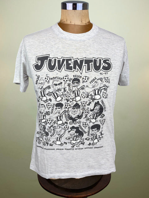 A light gray heather short-sleeve t-shirt displayed on a wooden dress form mannequin. The shirt features a large black graphic print with the word 'JUVENTUS' in a bold retro font, above a dense cartoon illustration of soccer players, balls, and fans.