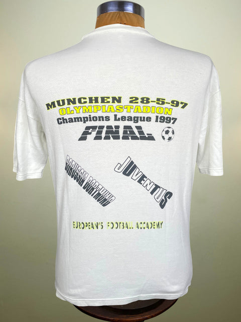 White short-sleeve t-shirt displayed on a mannequin, showing the back with yellow and black graphic text celebrating a 1997 Champions League final in München at Olympiastadion, featuring Juventus branding.