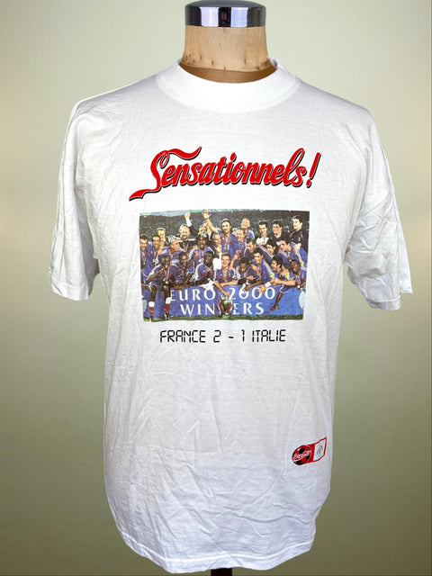 A white short-sleeve graphic t-shirt displayed on a wooden mannequin torso. The shirt features a red 'Sensationnels!' script across the chest, a central photo print of a soccer team in blue uniforms celebrating, and black text reading 'EURO 2000 WINNERS FRANCE 2 - 1 ITALIE' below.