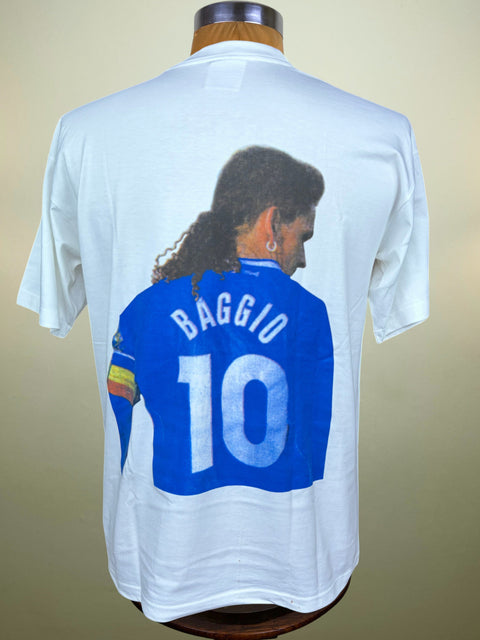 A white short-sleeve t-shirt displayed on a wooden mannequin torso, showing the back side with a large graphic print of a soccer player wearing a blue jersey with 'BAGGIO 10' on it.