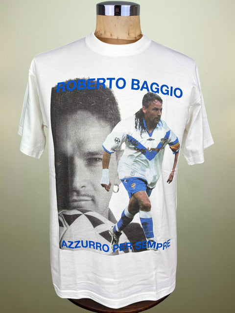A white short-sleeve graphic T-shirt displayed on a mannequin torso against a plain light background. The shirt features a large front print with a black-and-white portrait, a photo of Roberto Baggio in a blue-and-white soccer jersey, and blue text reading 'ROBERTO BAGGIO' and 'AZZURRO PER SEMPRE'.